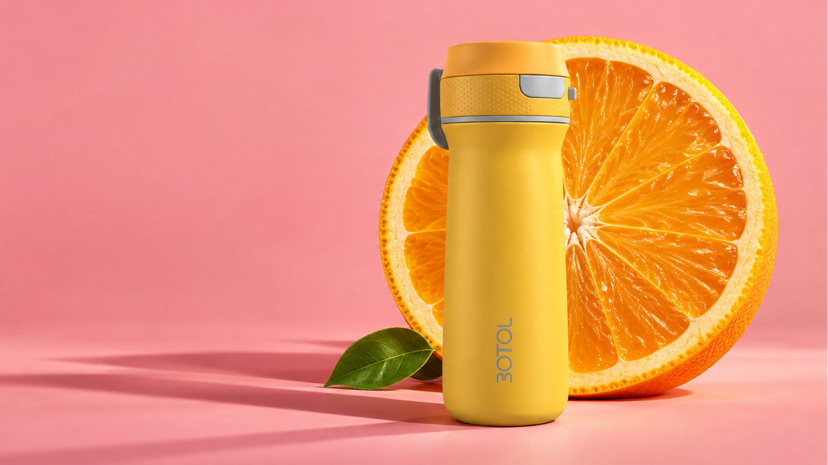 A yellow 3OTOL insulated water bottle with a gray lid accent, standing next to a sliced orange on a pink background with the 3OTOL logo in the top left.